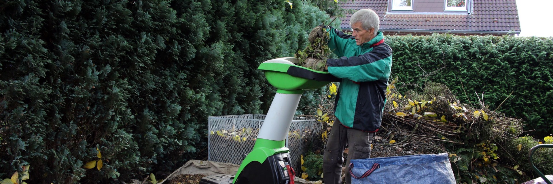 Mann häckselt mit einem Häcksler Äste klein als Grundlage für einen Komposthaufen