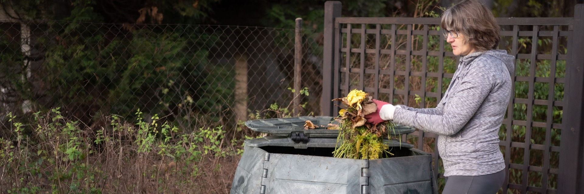 Frau wirft Laub und Rasenreste in den Komposter. Laub vom Kompost wird zum nährstoffreichen Humus.